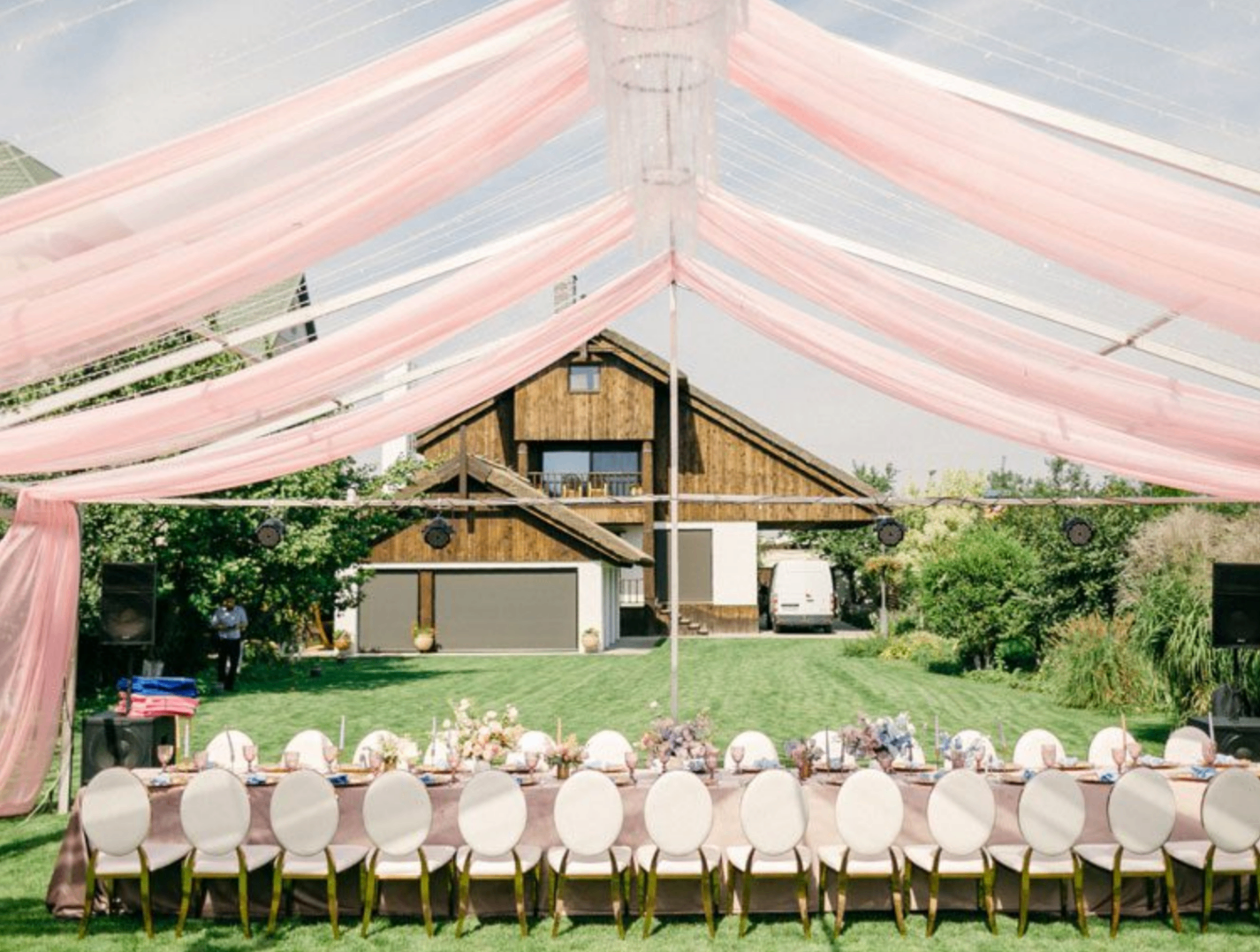 Long banquet table under clear tent with pink drapes and gold chairs
